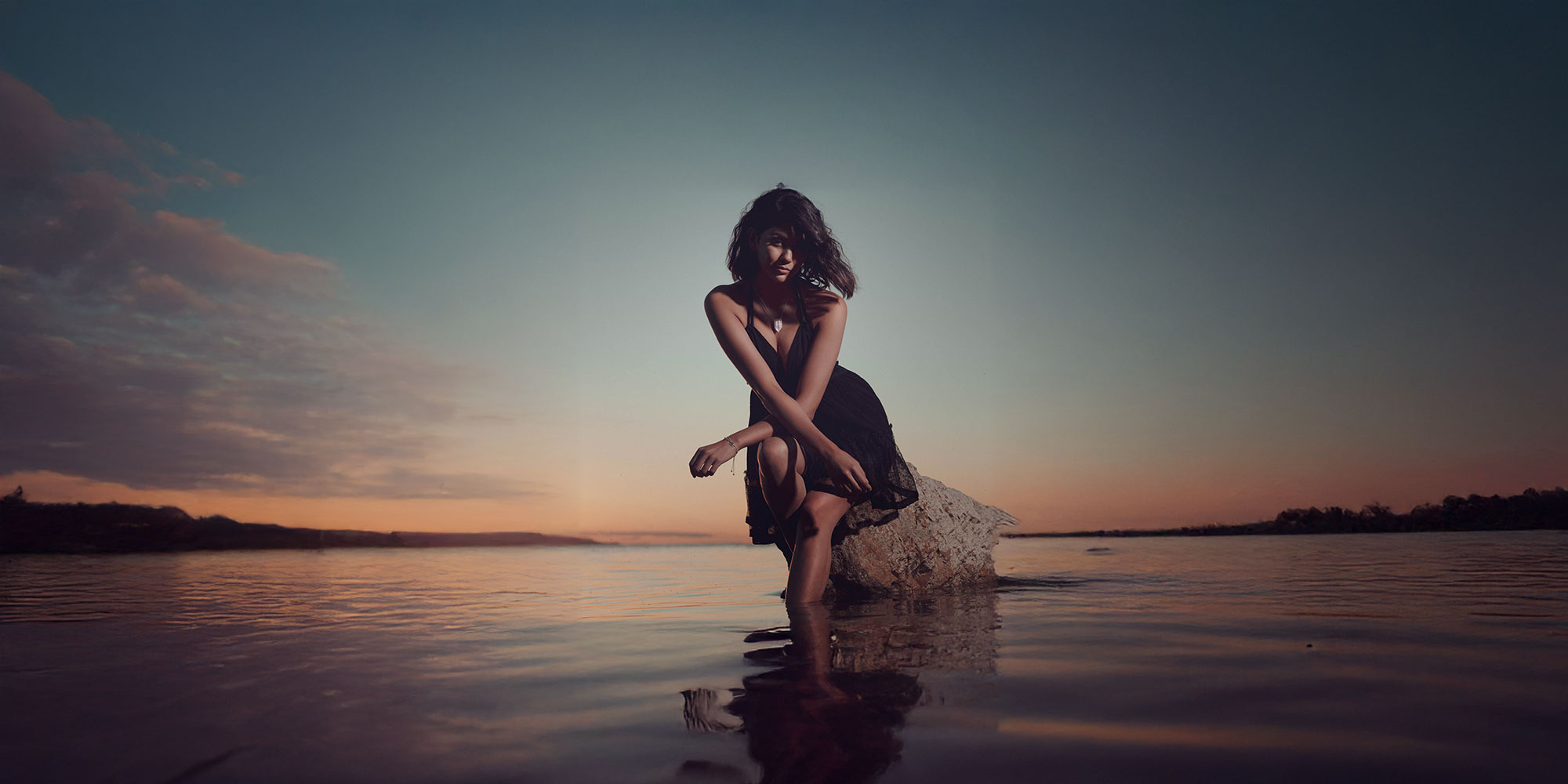 Fashion model by water at sunset